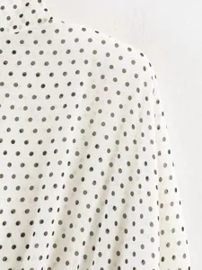 Detailed view of women's white blouse featuring classic black polka dot pattern and soft fabric.