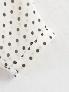 Close-up detail of women's polka dot top sleeve, featuring stylish print and button accent.