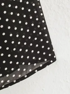 Detail shot of black and white polka dot chiffon fabric with curved hem for women's apparel.