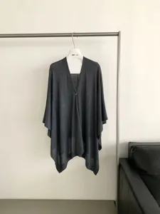 Vista dettagliata del cardigan poncho in maglia grigio scuro con bottone e drappeggio.