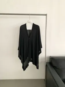Dettaglio in primo piano dello scialle cardigan in maglia nera, con orlo irregolare e bottone.
