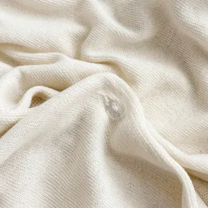 Primo piano della texture del tessuto in maglia crema e dettaglio del bottone.