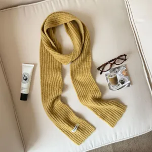 Close-up detail of a cozy yellow ribbed knit scarf styled with aesthetic props on a couch.