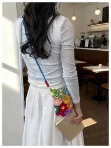 Sac de téléphone artisanal en crochet à fleurs colorées porté en travers dans un café.