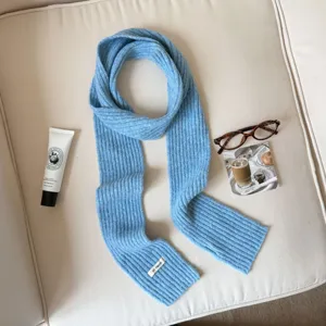 Detail view of a cozy light blue knit scarf with ribbed design and stylish label tag.