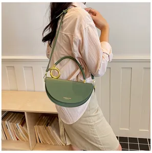 Grüne halbrunde Satteltasche im Detail, mit auffälligem Metallringgriff und elegantem Gürtel.