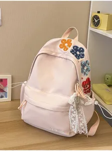 Nahaufnahme des rosa Schülerrucksacks mit bestickten Blumenaufnähern und Spitzenanhänger.