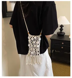 Artistic woven phone bag with long tassels and shell details worn as a crossbody bag