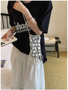Detail view of a white woven fringe phone bag worn crossbody in a lifestyle setting.