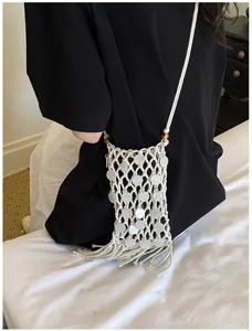 Artistic woven white phone bag with tassels and shell details on a black shirt