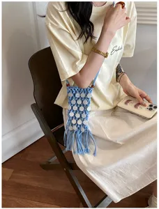 Close-up view of a light blue woven hollow phone bag with white disk accents and tassels