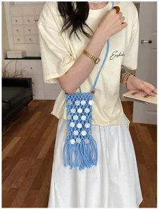 Detailed view of a blue woven crossbody phone bag with shell sequins and long tassels on model