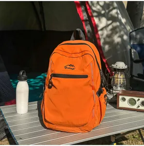 Sac à dos de randonnée orange présenté dans un décor de camping avec des accessoires