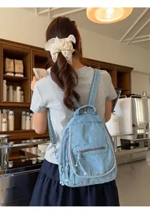 Back view of a vintage light blue washed denim backpack worn in a cozy cafe setting