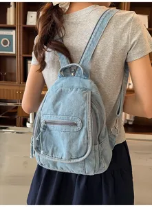 Back view of a woman wearing a light blue washed denim backpack in a cafe setting.