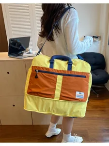 Detail of a large yellow and orange color-block travel bag carried by a woman in white.