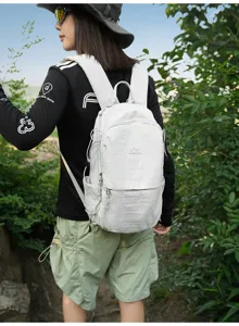 Randonneuse portant un sac à dos compact en nylon gris clair sur un sentier de forêt.