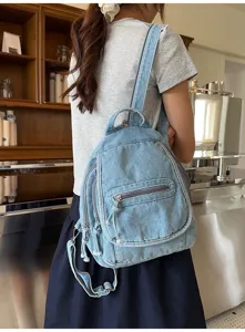 Detailed view of a vintage washed denim backpack worn by a model in a cafe setting