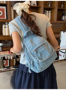 Lifestyle detail of a light blue denim sling backpack worn by a model in a cafe