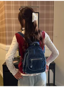 Rear view of a vintage washed denim backpack worn by a model in a stylish indoor setting