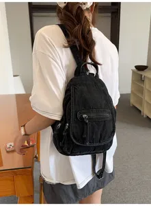 Woman wearing a vintage black washed denim backpack in a modern indoor lifestyle setting