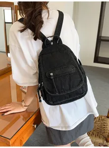 Vintage black washed denim backpack for women worn on the back in a casual indoor setting