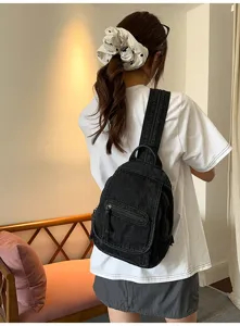 Rear view of a stylish black washed denim backpack worn by a model in a cozy room