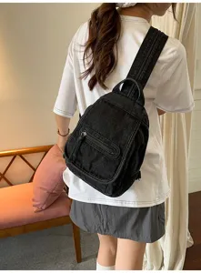 Detailed view of a vintage washed black denim sling backpack worn by a model indoors