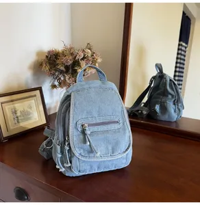 Retro washed denim backpack for women showing front and side detail on a wooden desk
