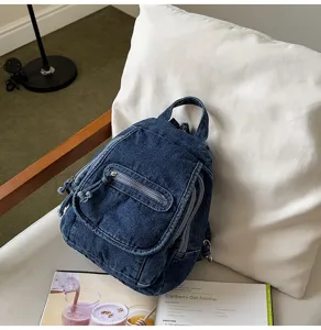 Close-up of vintage washed denim backpack featuring multiple zipper compartments