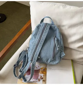 Detailed back view of a retro blue washed denim backpack placed on a white pillow and chair