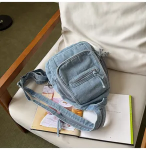 Vintage washed denim chest bag with multiple zippers shown on a lifestyle chair.