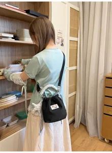Dettaglio della borsa a secchiello nera che mostra l'unico manico bianco e la chiusura a coulisse