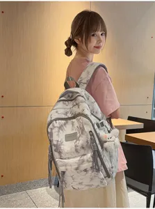 Asian student wearing a trendy large capacity tie-dye backpack with cute plush pendant.