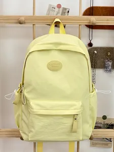 Nahaufnahme eines pastellgelben Rucksacks mit rundem Mode-Patch an einer Holzstange.