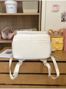 Vista dettagliata di uno zaino Itabag bianco su una scrivania con materiale scolastico.