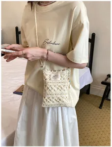 Close-up of a handmade cream crochet phone bag worn with a casual pale yellow t-shirt