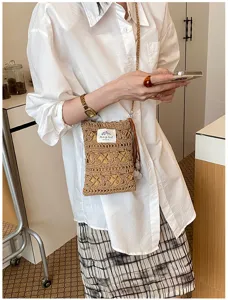 Detail view of a hand-woven straw phone bag styled with a white shirt and plaid skirt.