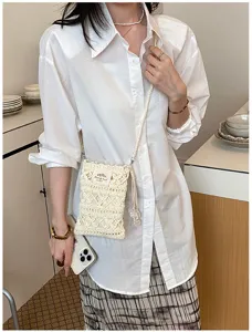 Detail view of a cream handmade crochet crossbody phone bag on a white shirt model.