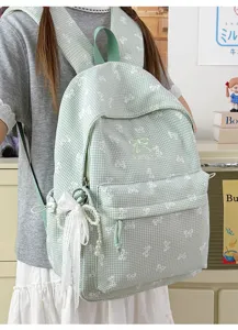 Détail d'un sac à dos d'école à carreaux verts avec nœuds mignons et pendentif en perles.