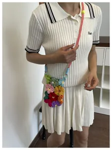 Gros plan d'un sac à bandoulière en fleurs tricotées main porté avec un polo blanc