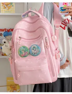 Gros plan d'un sac à dos rose avec motifs d'étoiles et pin's de personnages.