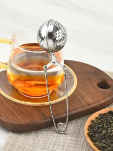 Détail d'infuseur à thé en inox avec boule à mailles fines et poignée de presse.