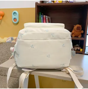 Detail eines süßen cremefarbenen Rucksacks mit hellblauer Schleifenstickerei im Zimmer