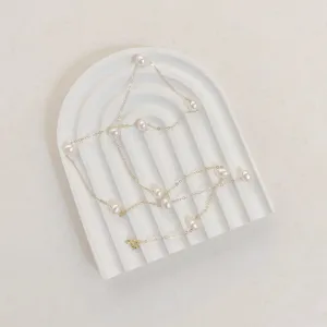 Elegant pearl necklace on white arch tray, minimalist jewelry photography display prop.