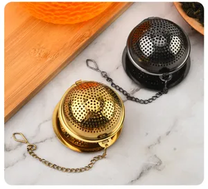 Vue détaillée d'une boule à thé en acier inoxydable montrant des boules dorées et noires avec chaînes.