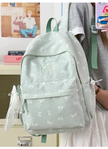 Gros plan d'un sac à dos vichy vert avec des motifs de nœuds blancs et charme en dentelle