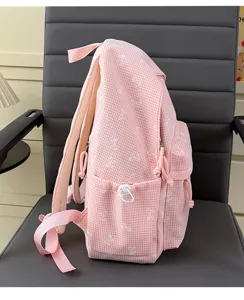 Vue latérale d'un sac à dos d'école à carreaux roses avec des motifs de nœuds blancs