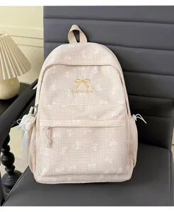 Détail d'un sac à dos à carreaux beige avec motifs de nœuds brodés et logo doré.