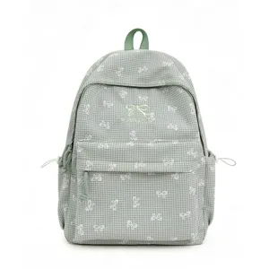 Vue détaillée du sac à dos vert à carreaux avec motifs de nœuds blancs et broderie